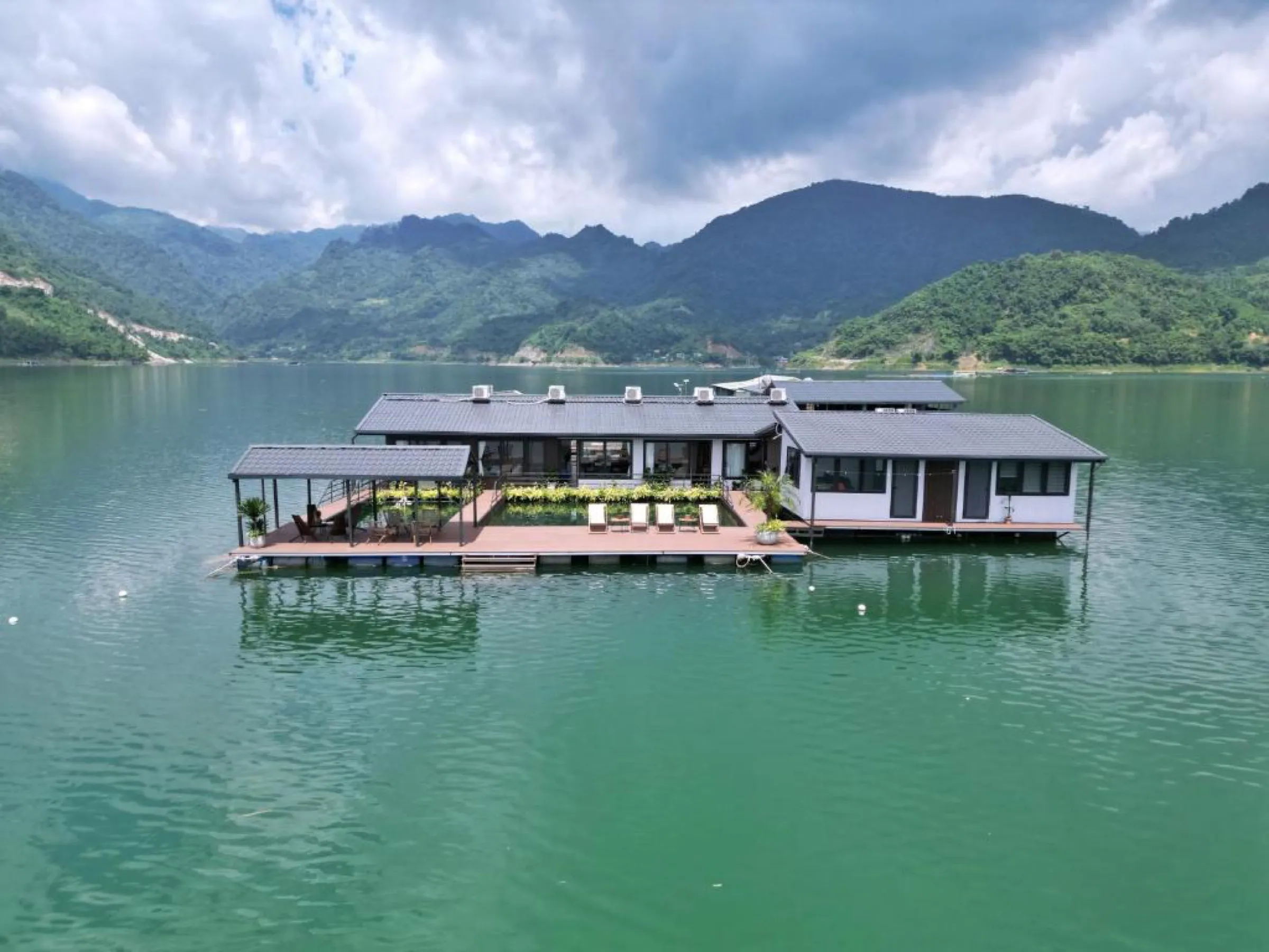 A private floating house moored on the calm green water of Hoa Binh Lake, mountains behind.