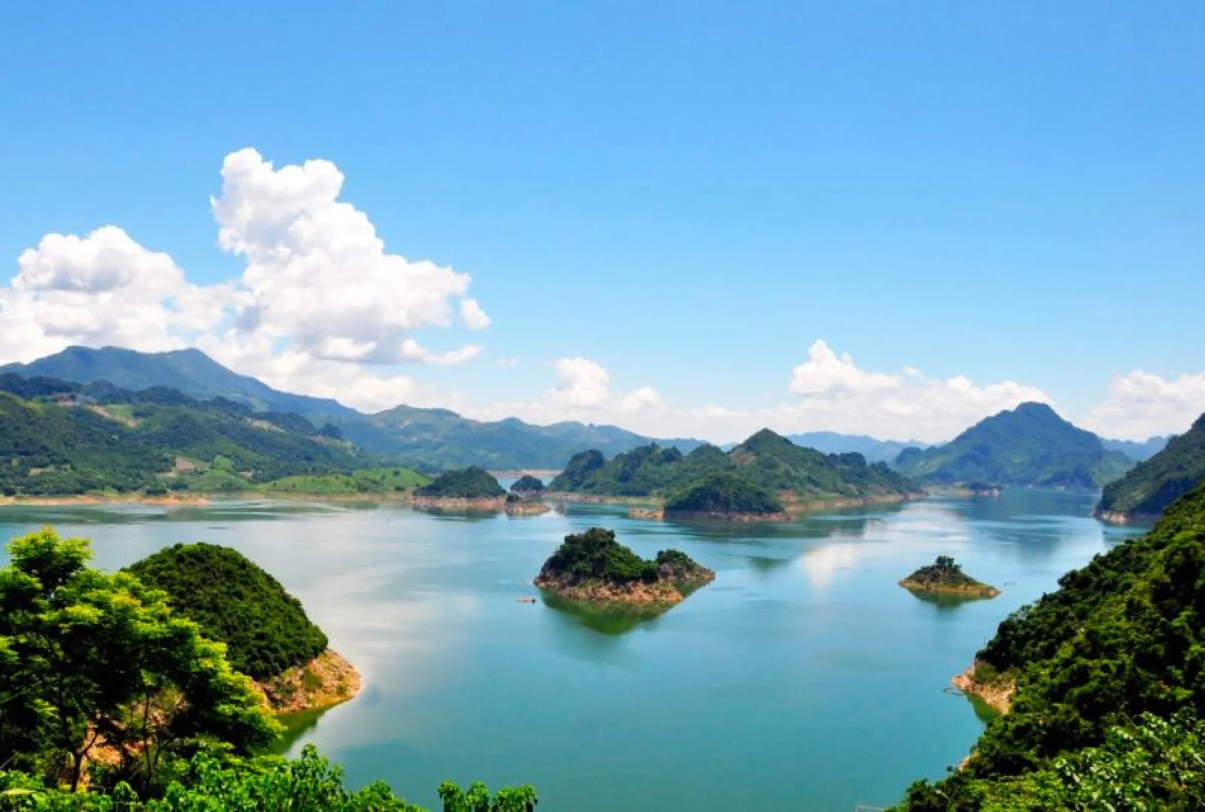 Limestone islands scattered across the turquoise water of Hoa Binh Lake under a blue sky.