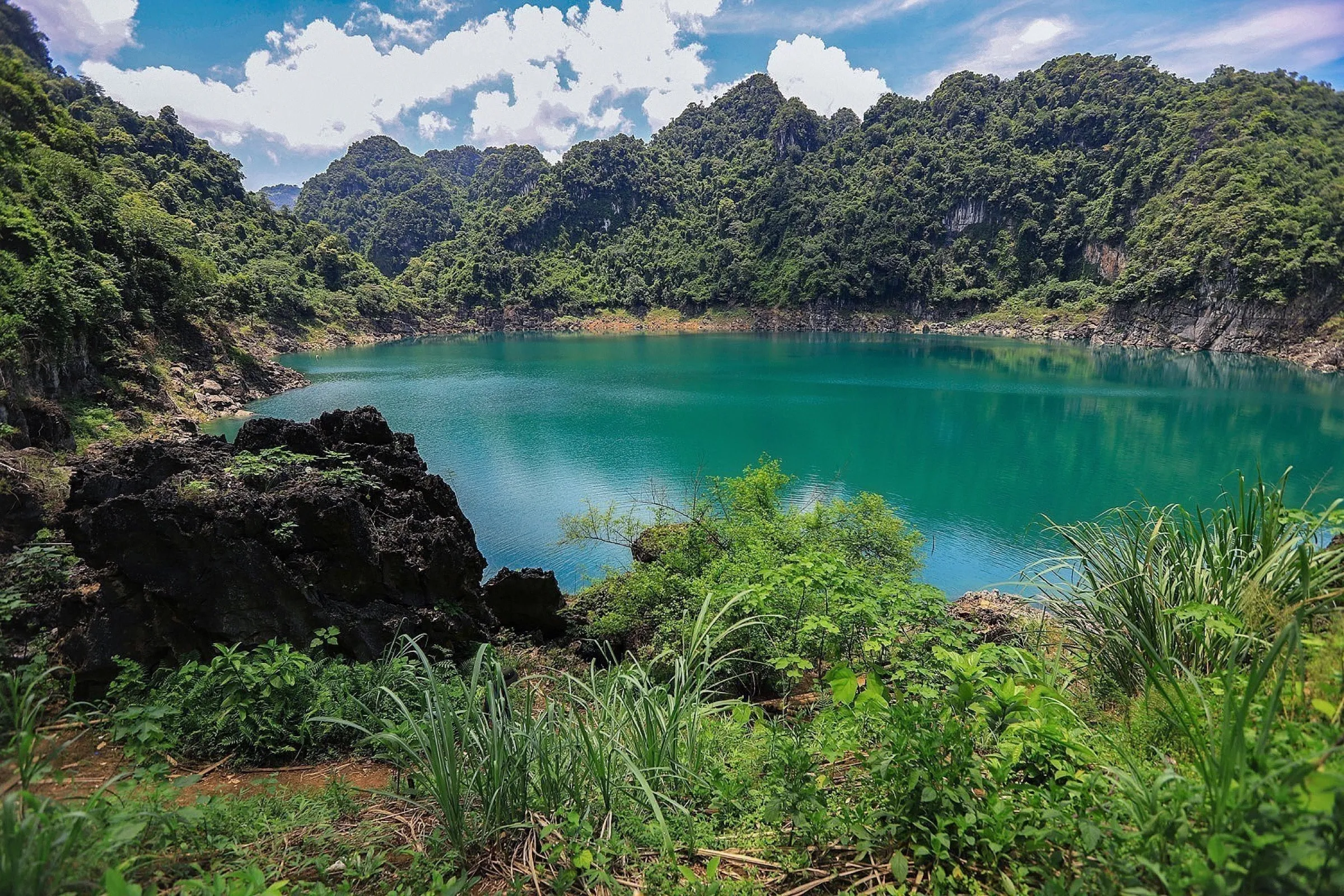 The emerald water of the Dragon Eye Lake ringed by limestone cliffs and forest.