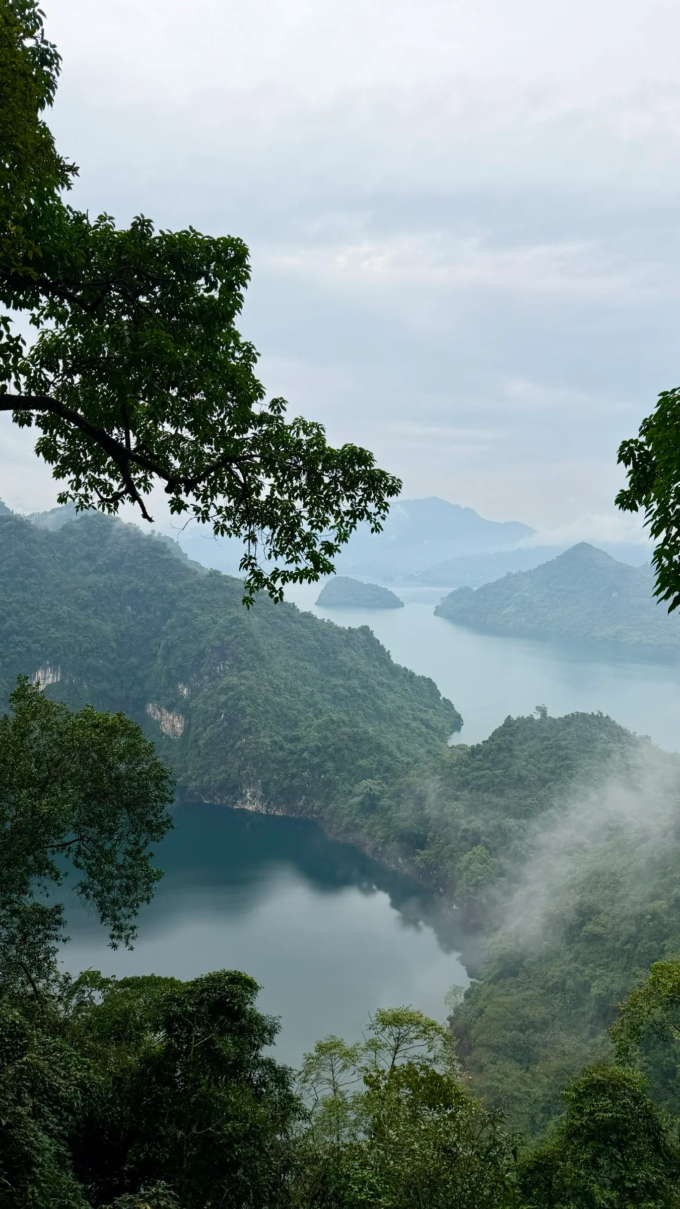 Misty arms of Hoa Binh Lake winding between forested limestone hills at dawn.