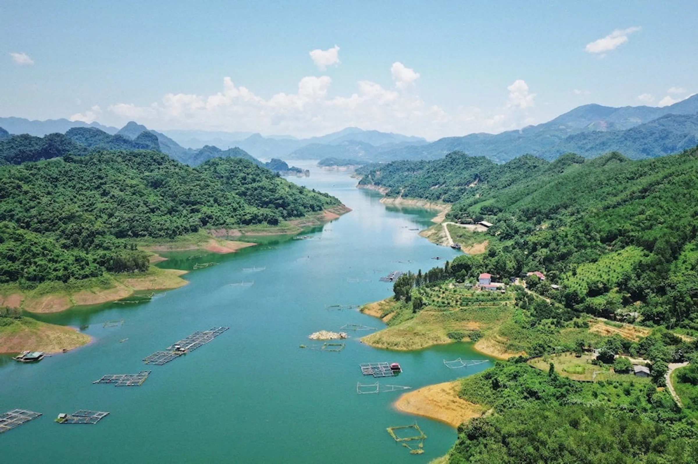 Aerial view of fish farms and a quiet arm of Hoa Binh Lake ringed by green hills.