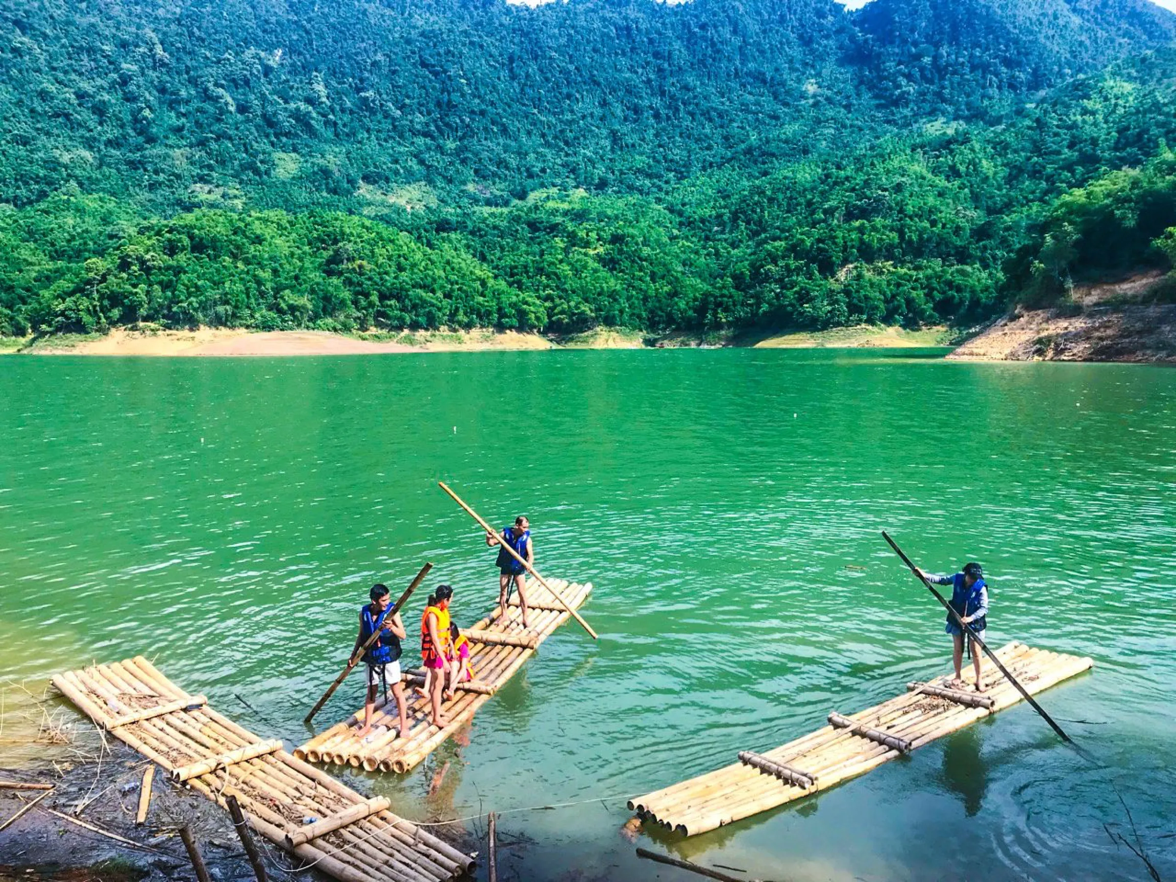 Travellers crossing the green lake on traditional bamboo rafts.